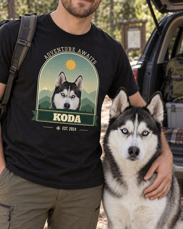 Adult beside an open car boot with a black-and-white husky, wearing a black adventure photo tee with the same dog in a mountain arch and the name Koda.
