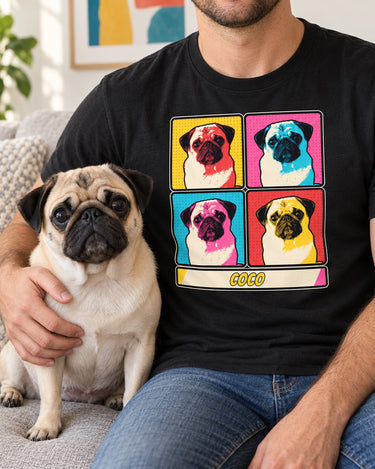 Adult seated beside a fawn pug in a bright room, wearing a black pop art pet portrait shirt with the same pug repeated in four colorful panels.