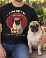 Torso view of an adult in a black COCO pet varsity tee with the same fawn pug seated alongside in a backyard, showing the oval collegiate portrait patch.