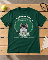 Forest green KODA pet varsity shirt laid on a wooden gym bench beside a tennis ball, whistle and plain pennant, with green and white artwork.