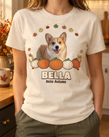 Natural cream personalized fall pet shirt worn in a warm kitchen, with the name BELLA, a dog portrait, orange pumpkins and a hanging autumn leaf garland.