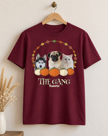 Maroon Thanksgiving pet photo shirt on a wooden hanger, showing three pets inside a leaf wreath above pumpkins, THE GANG lettering and Thankful below.