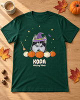 Forest green Witchy pet photo shirt laid on an oak table beside leaves, acorns and a mug, with a husky in a purple witch hat above pumpkins and KODA.