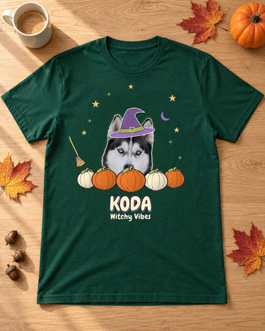 Forest green Witchy pet photo shirt laid on an oak table beside leaves, acorns and a mug, with a husky in a purple witch hat above pumpkins and KODA.