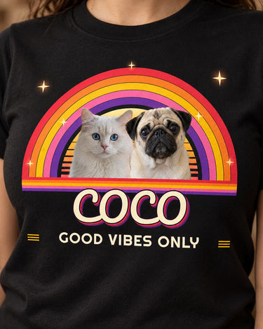 Close-up of the retro sunset print on a black t-shirt: a pug and a white cat in front of a striped sun and rainbow arcs with groovy script lettering