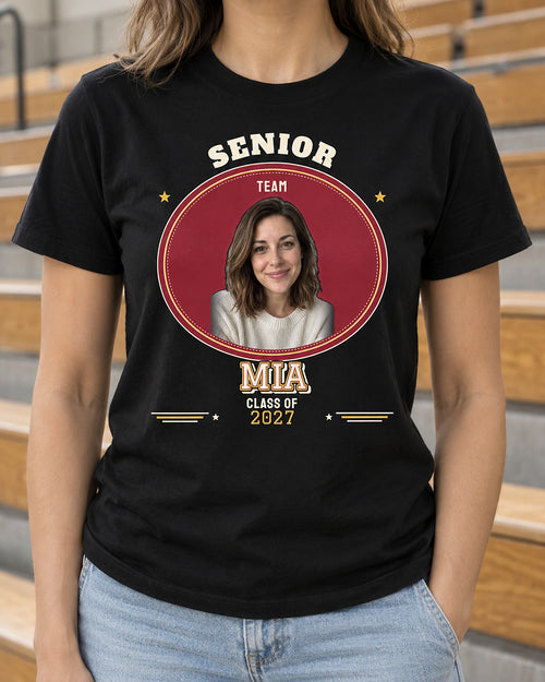 Black senior varsity photo shirt beside gym bleachers, with a portrait in an oval patch, cream MIA lettering and Class of 2027 below.