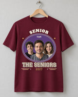 Maroon senior varsity shirt on a wooden hanger, with three portraits, purple and gold artwork, THE SENIORS lettering and a 2027 year row.