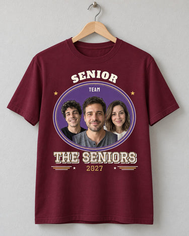 Maroon senior varsity shirt on a wooden hanger, with three portraits, purple and gold artwork, THE SENIORS lettering and a 2027 year row.