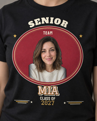 Close-up of a black MIA senior varsity tee, showing the portrait, cream block name with cardinal and gold outlines and printed stitch marks.