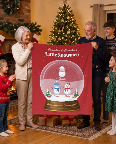 Personalized grandparents blanket with grandkids names, red snow globe design with little snowmen held up by grandma, grandpa and the grandkids by the Christmas tree