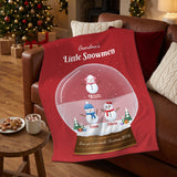 Little snowmen grandkids names blanket draped over a leather sofa next to hot cocoa and cookies