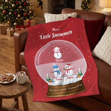 Mom's Little Snowmen personalized blanket with kids names draped over a leather sofa next to hot cocoa and cookies