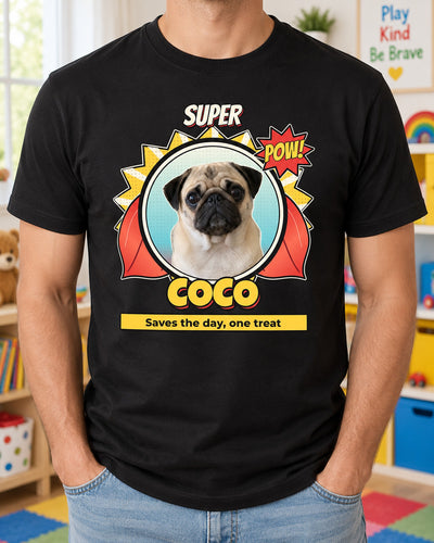 Black custom superhero dog shirt in a bright playroom, showing Coco the pug in a comic circle with a red cape, yellow burst and bold SUPER title.