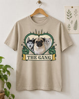Sand pet tattoo flash tee on a wooden hanger, with three pets inside a green heart, green roses, gold details and The Gang name scroll.