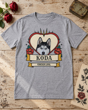Sport grey Koda tattoo pet tee laid on pale wood beside red roses, a vintage tin and botanical tattoo flash, with a red heart and teal leaves.