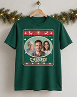 Forest green Christmas photo tee on a wooden hanger, showing three portraits, Cheers lettering and an Evergreen knit-style print