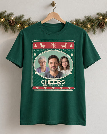 Forest green Christmas photo tee on a wooden hanger, showing three portraits, Cheers lettering and an Evergreen knit-style print