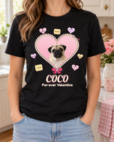 Black custom Valentine pet photo shirt worn with light-wash jeans in a cozy kitchen, showing Coco the pug inside a pink candy heart with a cream scalloped border.