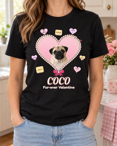 Black custom Valentine pet photo shirt worn with light-wash jeans in a cozy kitchen, showing Coco the pug inside a pink candy heart with a cream scalloped border.