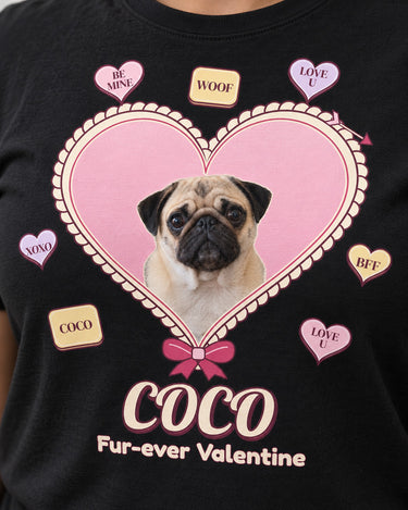 Close-up of the pastel Valentine print on a black shirt, showing Coco the pug, the cream scalloped heart edge, conversation candies, bow and script name.