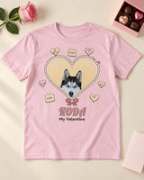 Light pink Koda pet Valentine shirt laid on a cream table beside a rose, chocolates and a plain card, with a gold heart and rose ribbon accents in the print.