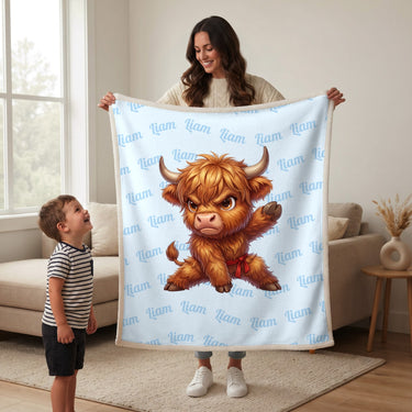 Mother holding up a baby blue karate Highland cow blanket with the name Liam for a smiling boy
