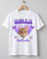 White Y2K pet photo t-shirt on a wooden hanger with an orange tabby cat in a lilac rhinestone heart, glittery butterflies and the name Bella